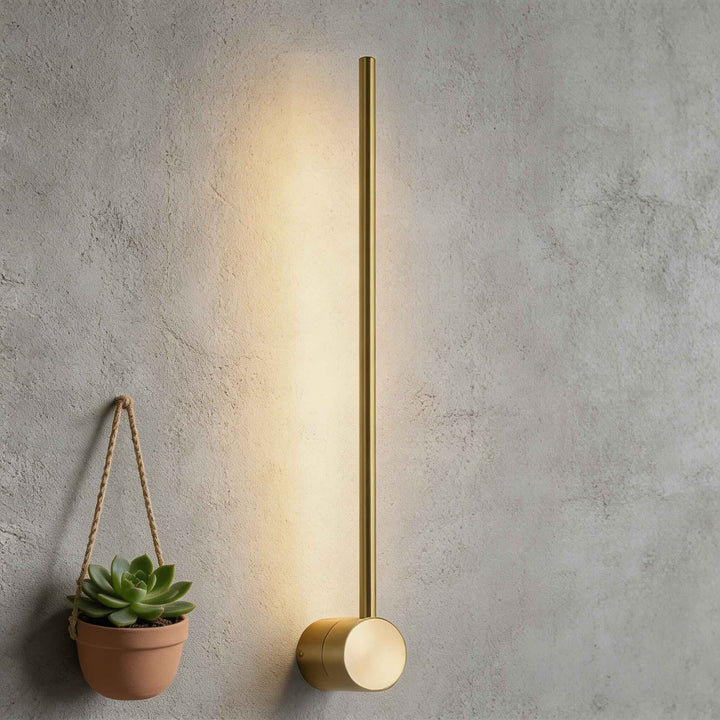 Wall sconce in brushed gold with slim vertical rod and round base, modern LED wall light with warm ambient glow and minimalist style