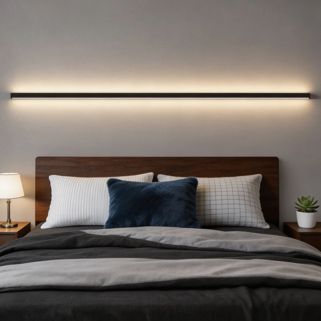 Long black linear LED wall sconce above bed with warm white glow, modern bedroom wall light Australia