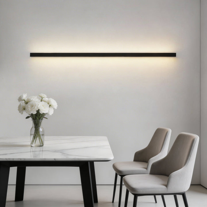 Matte black long linear LED wall sconce with warm white glow over marble dining table, modern wall light Australia